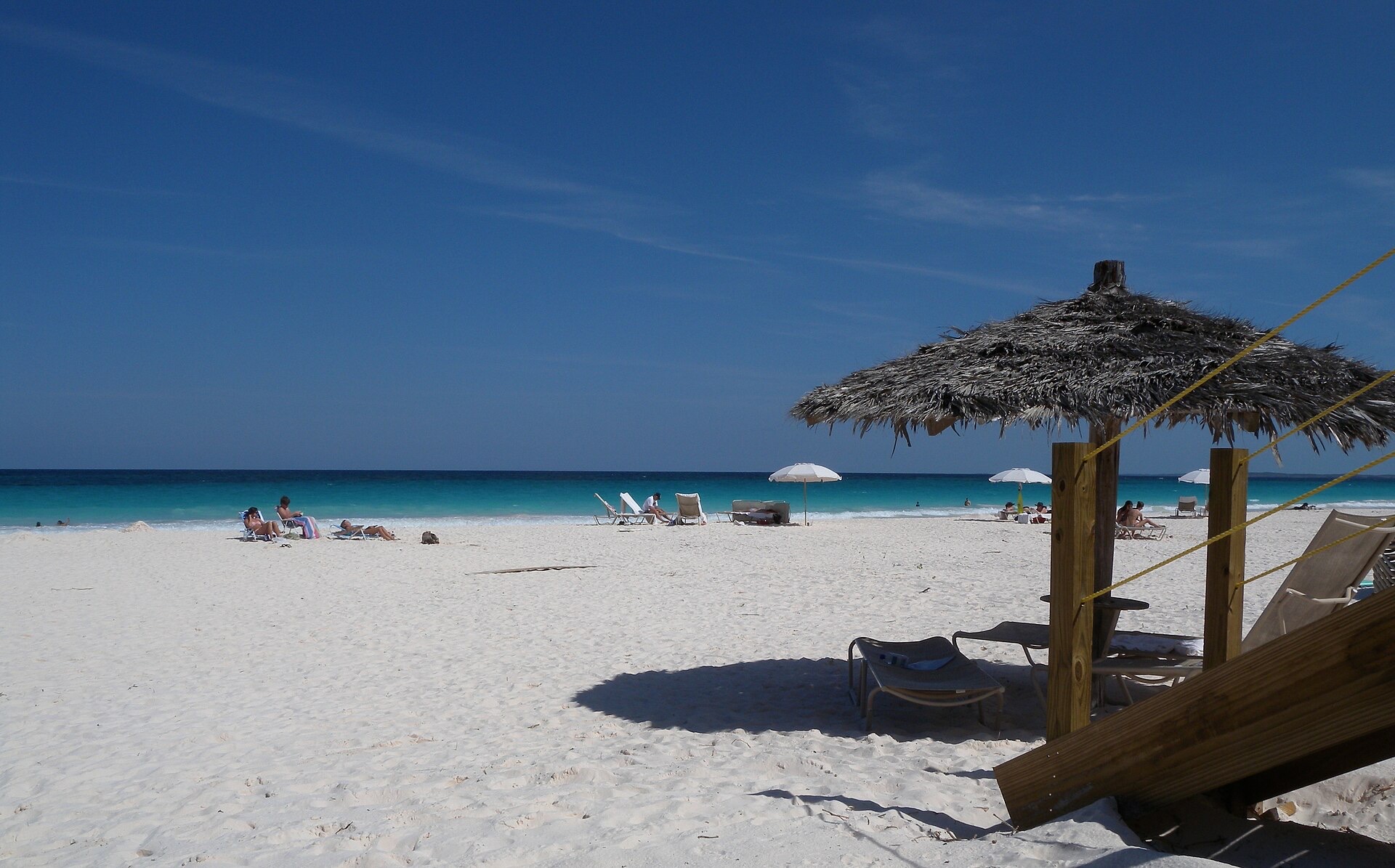 Pink Sands Beach on Harbour Island, Bahamas, with sun loungers under a thatched palapa and turquoise water